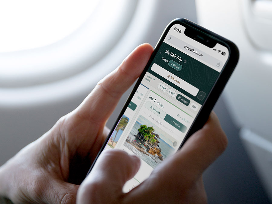 A person holding a smartphone by an airplane window, browsing their Bali Rivo itinerary builder for a Bali trip on a website, with travel details and images visible on the phone screen.