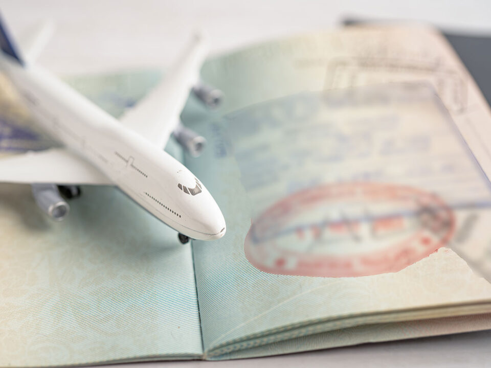 A small toy airplane rests on an open passport, with visible entry and departure stamps. The image symbolizes travel and international journeys.