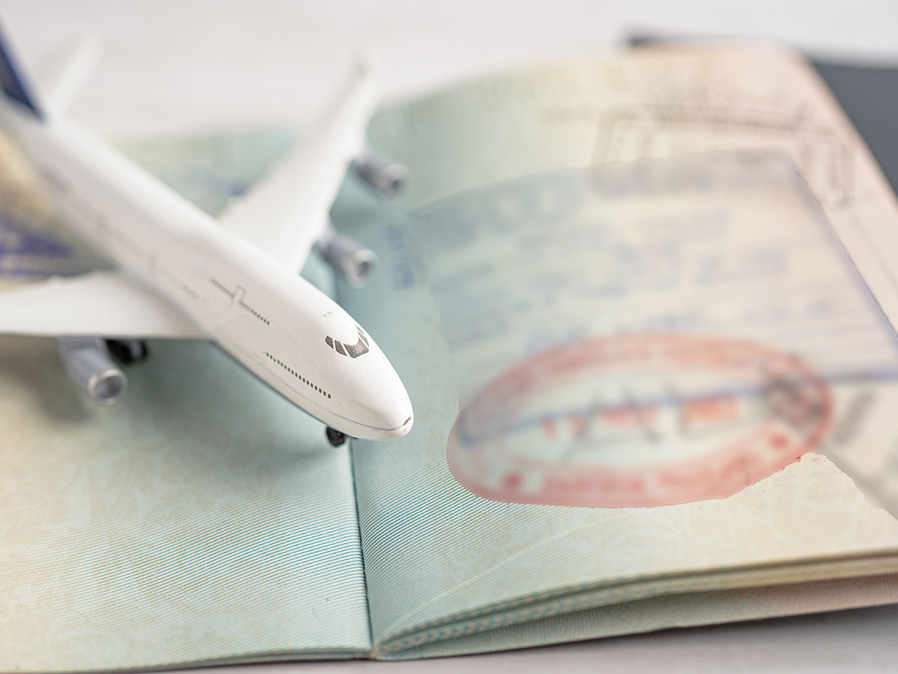 A small toy airplane rests on an open passport, with visible entry and departure stamps. The image symbolizes travel and international journeys.